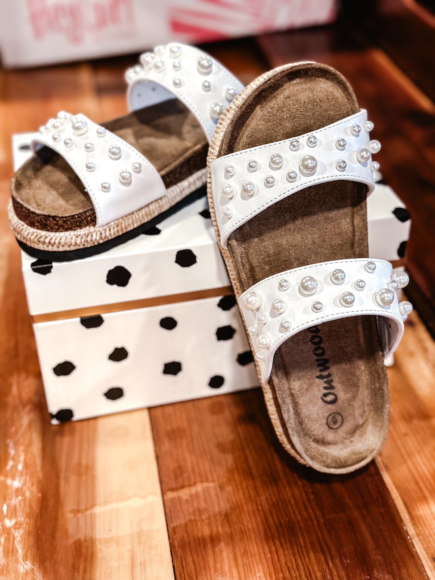 A pair of white Outwoods-topaz 4 sandals with double straps and studded details, displayed on a polka dot box.
