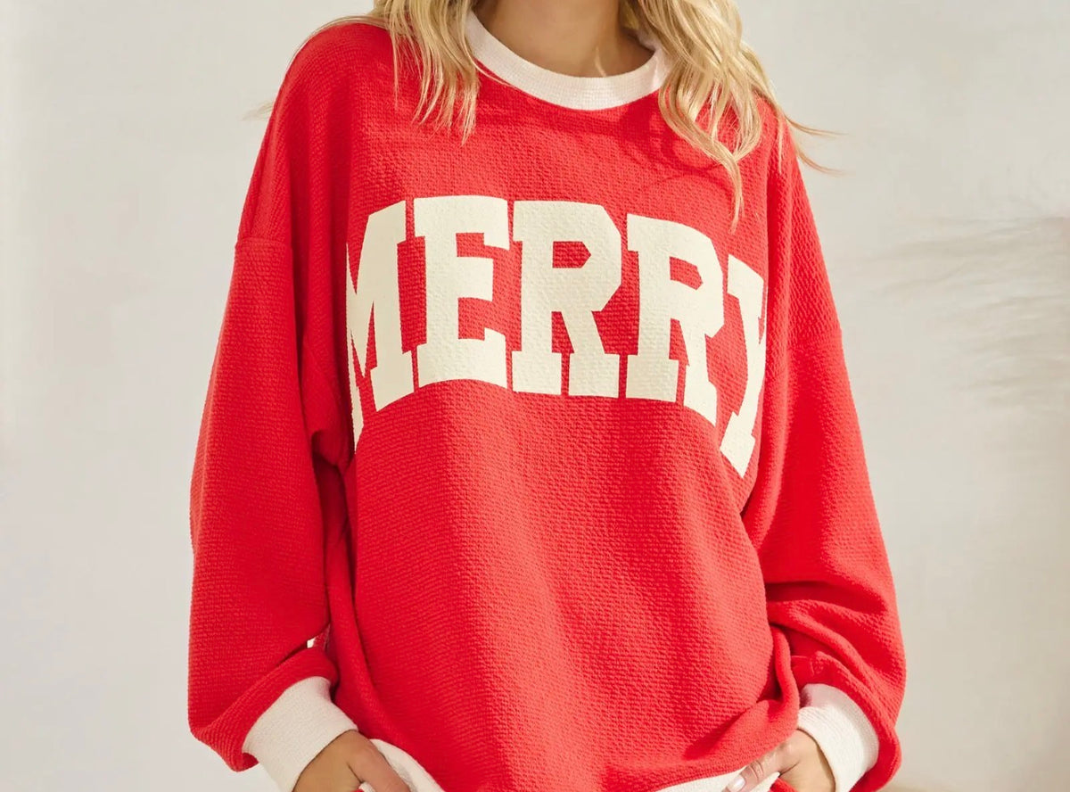 Women's red Merry Christmas pullover with oversized cream lettering and contrast trim.