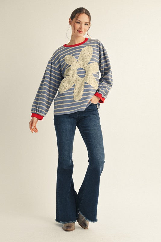 Woman wearing a striped sweater with a large flower design and blue jeans on a beige background