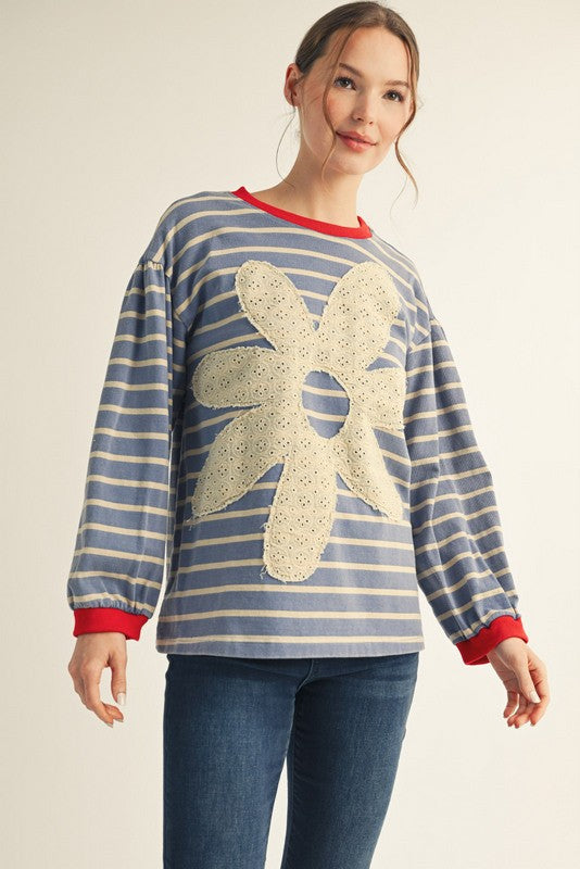 Woman wearing a blue and white striped sweater with a large beige flower design on a plain background