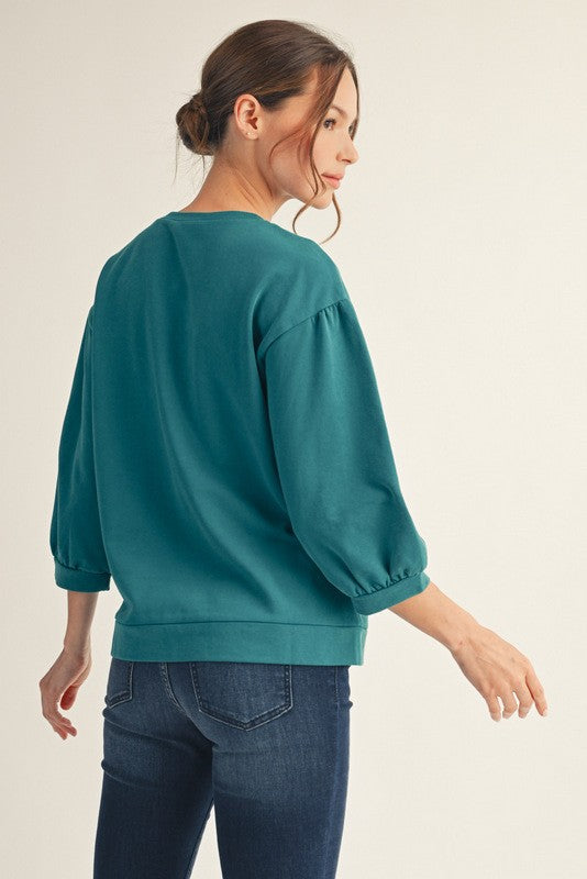 Woman wearing a teal sweater and blue jeans on a beige background