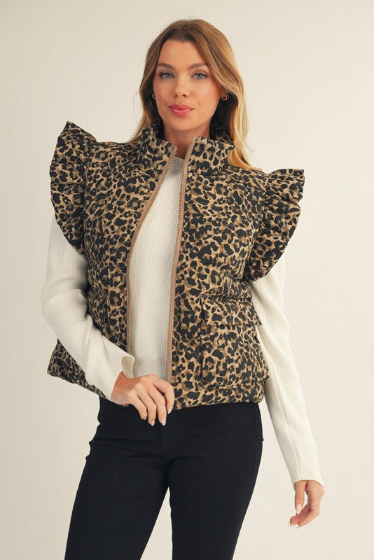 Woman wearing a leopard print vest over a white shirt and black pants on a plain background