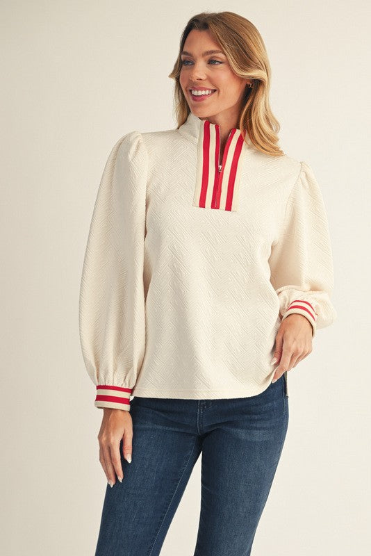 Woman wearing a cream blouse with red accents and blue jeans on a beige background