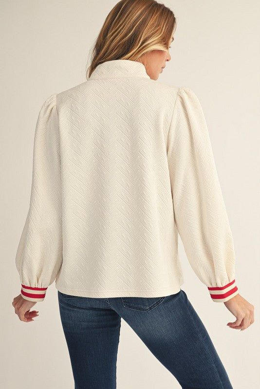Woman wearing a cream-colored sweater with red trim on a plain background