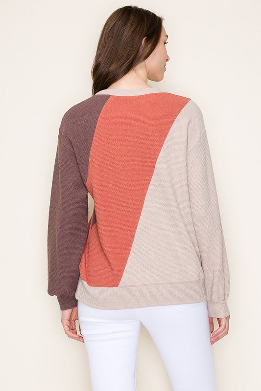 Woman wearing a color-blocked sweater with brown, red, and beige sections on a plain background