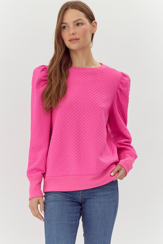 Woman wearing a bright pink textured sweater and blue jeans on a white background