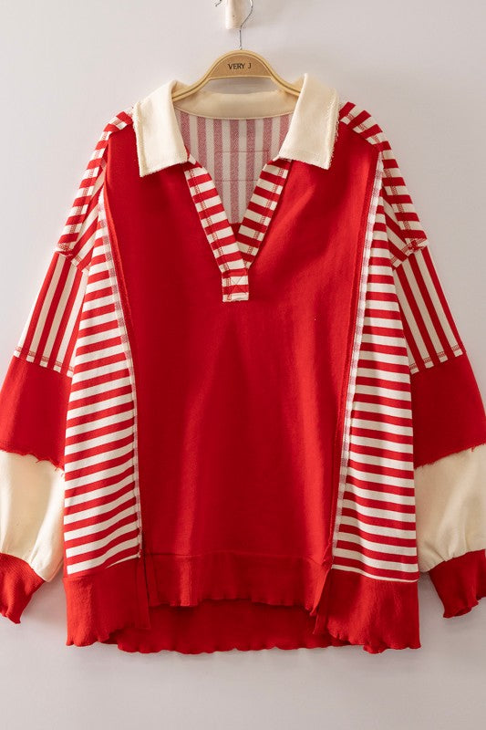 A red long-sleeve top with cream-colored collar, cuffs, and striped sleeves, hanging on a wooden hanger against a light gray wall.