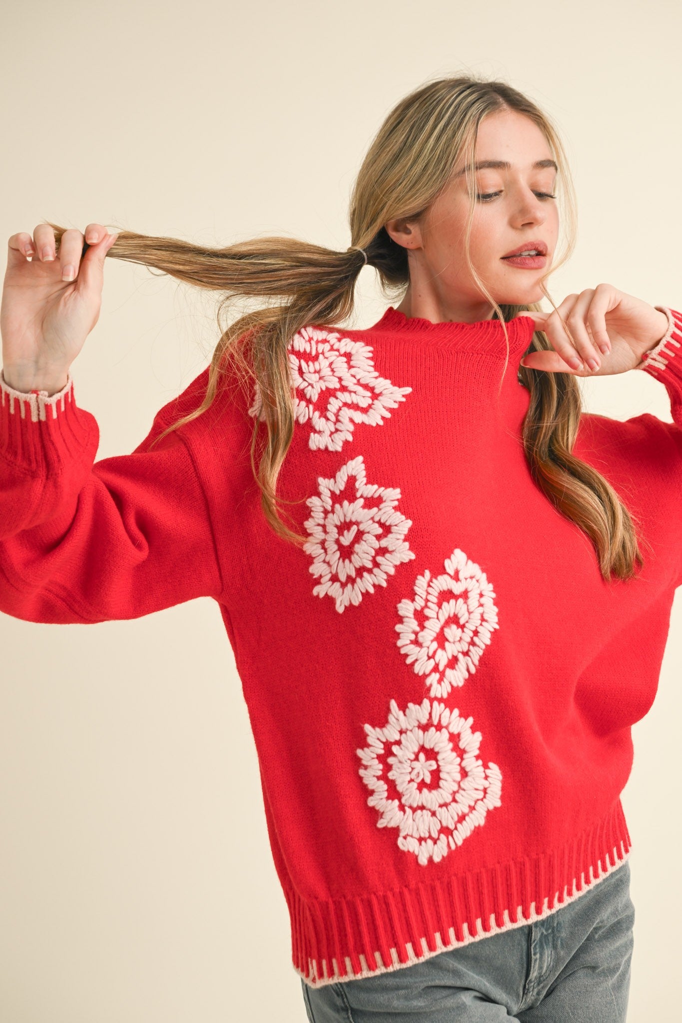 Woman wearing a red sweater with white floral patterns, holding her hair.