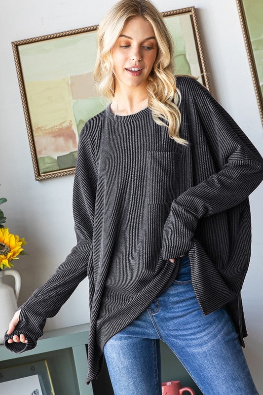 Woman wearing a dark gray oversized sweater and blue jeans indoors with framed artwork on the wall.