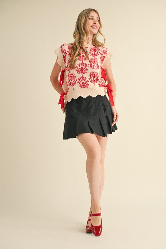 Woman wearing a floral top and black skirt with red shoes on a beige background