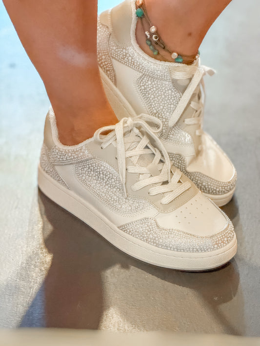 White sneakers with rhinestone embellishments on a reflective surface.