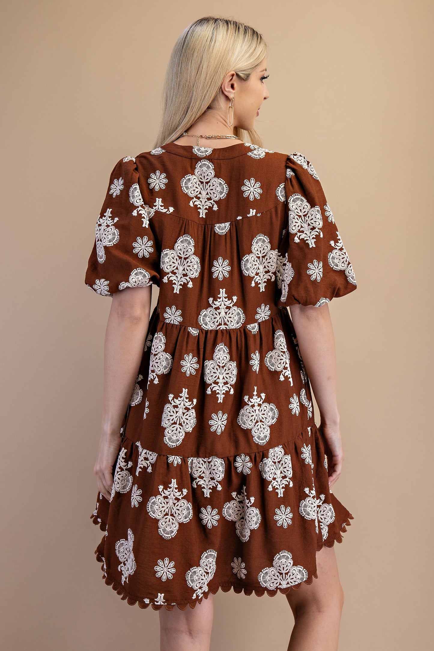 Woman wearing a brown dress with white floral patterns on a beige background