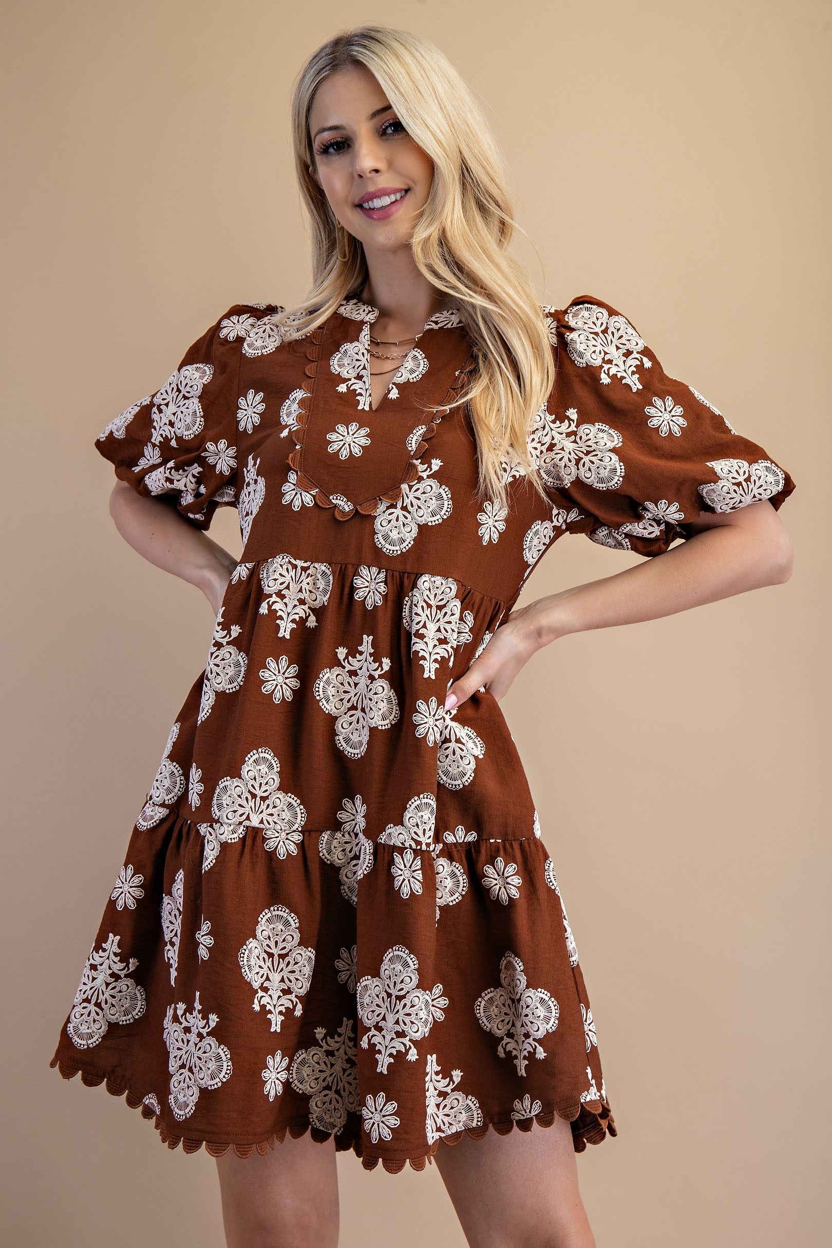 Woman wearing a brown dress with white floral patterns against a beige background