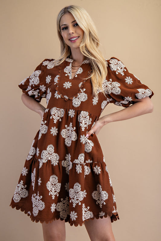 Woman wearing a brown dress with white floral patterns against a beige background