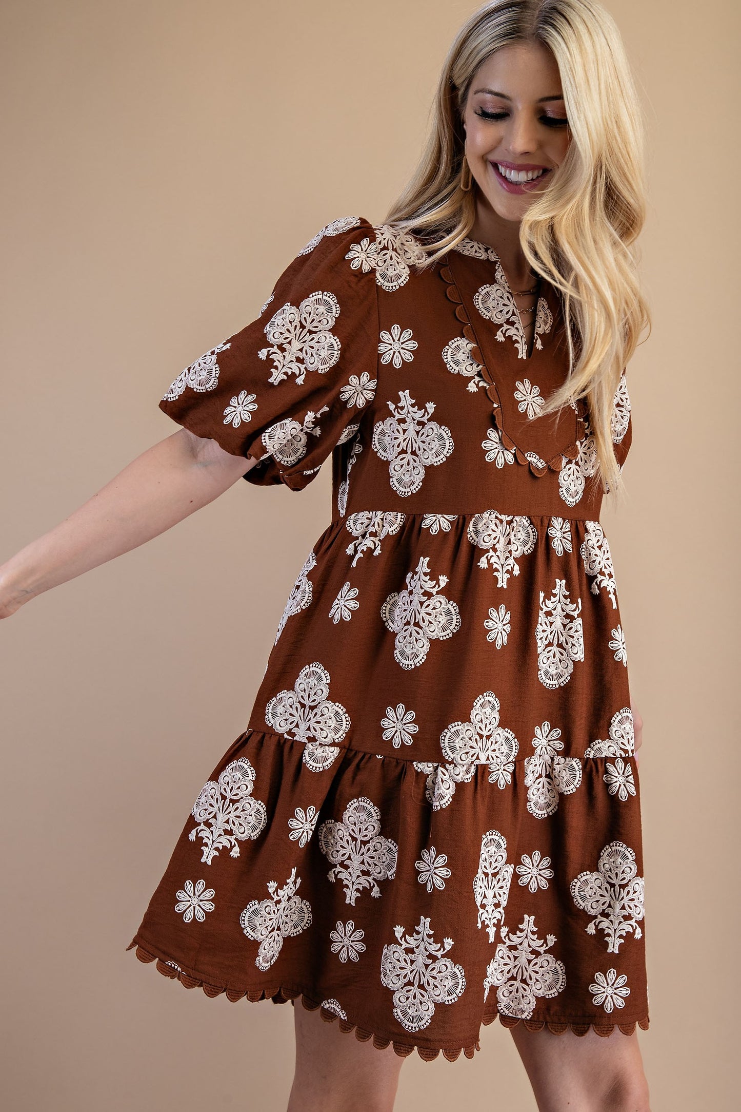 Woman wearing a brown dress with white floral patterns on a beige background