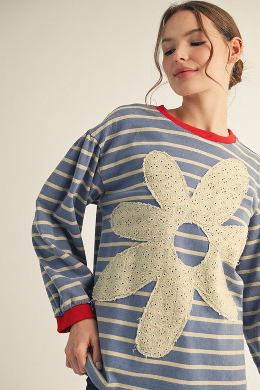 Woman wearing a blue and white striped sweater with a large beige flower design on a plain background