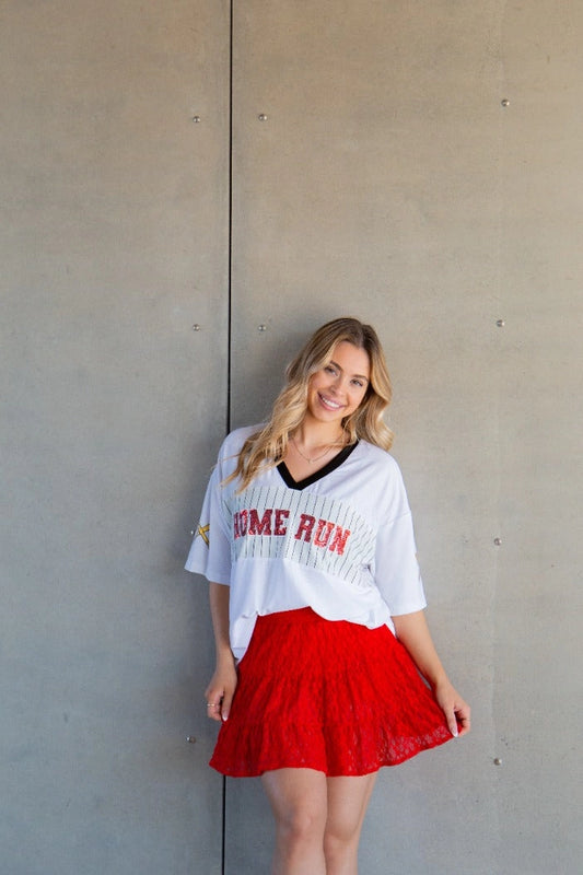 Woman wearing a relaxed fit Home Run sequin jersey top with V-neck and sparkly baseball lettering styled with skirt.
