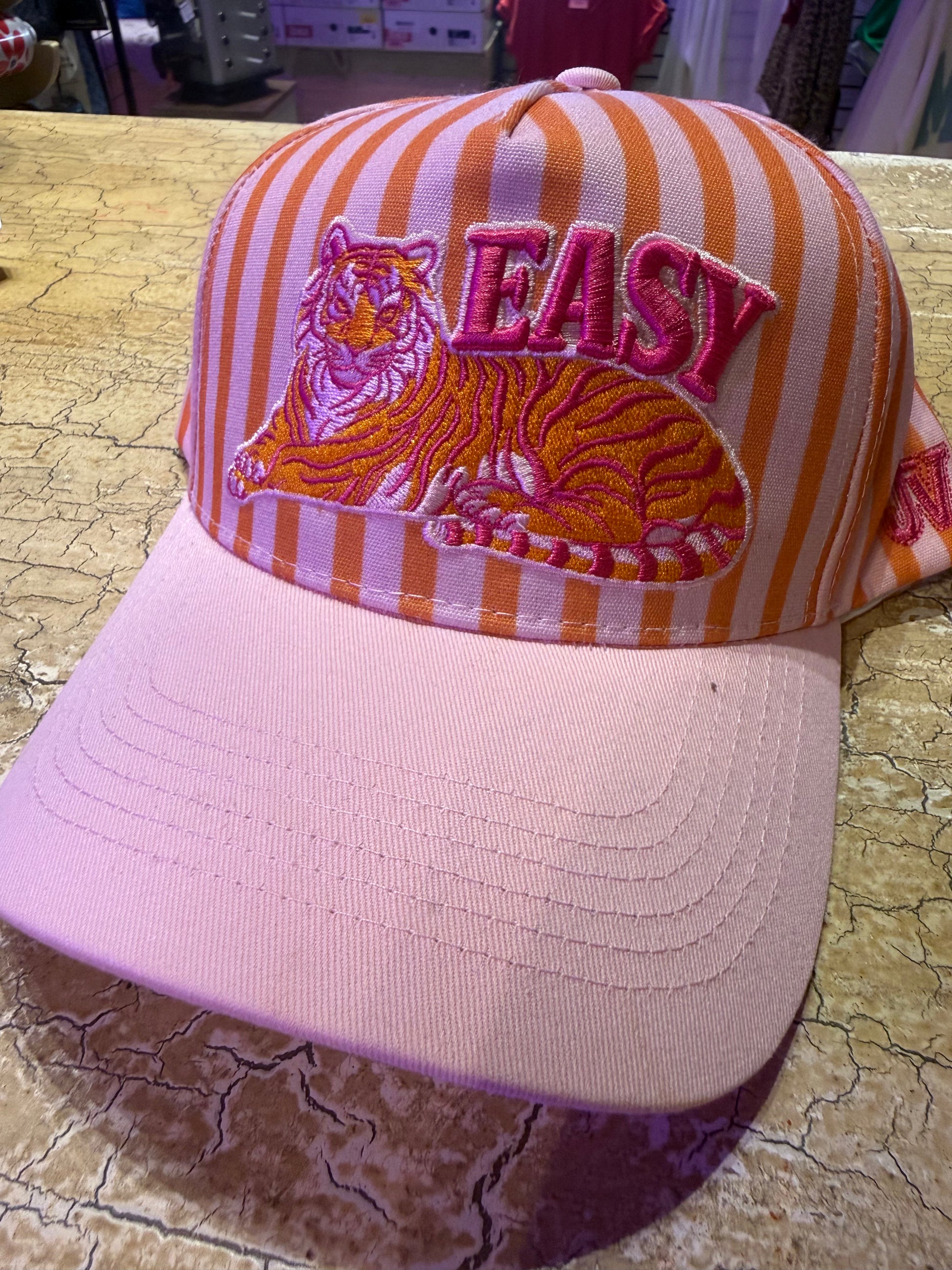 Pink and orange striped cap with tiger design and 'EASY' text on a textured surface.