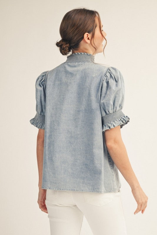 Washed denim puff sleeve top with smocked standing neckline and solid contrast detail.
