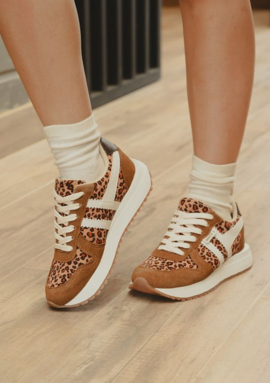 Brown sneakers with leopard print pattern worn indoors on a wooden floor.