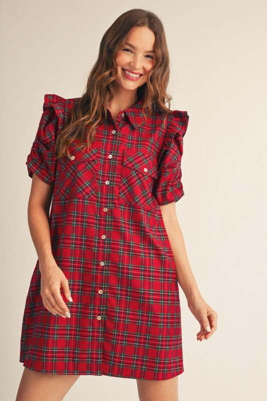 A woman modeling a red plaid mini dress with ruffled short sleeves, a button-front collar, and chest pockets against a plain light beige studio background.