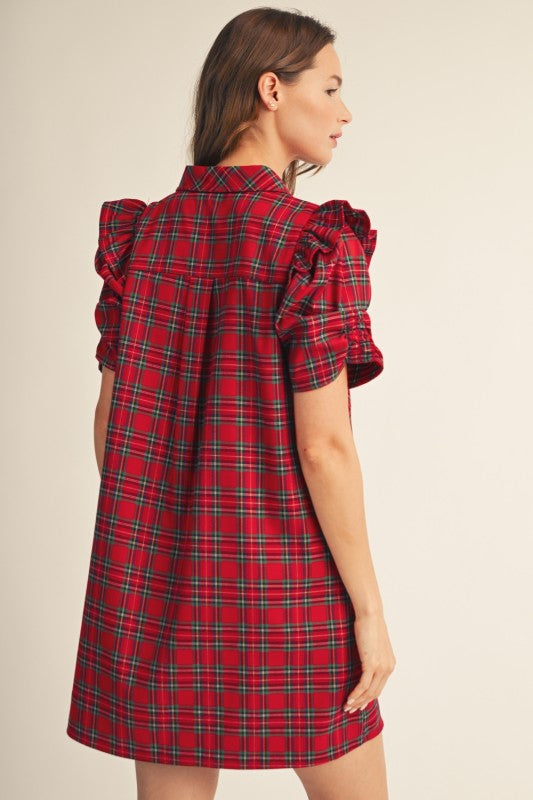 A woman wearing a red tartan plaid mini dress with ruffled short sleeves, shown from a side-back angle against a plain beige studio background.