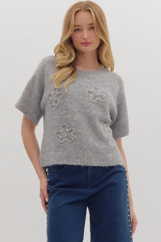Woman wearing a gray sweater with floral embellishments on a plain background