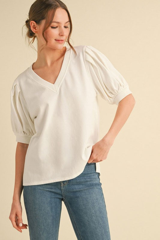 Woman wearing a white blouse with puff sleeves and blue jeans on a beige background