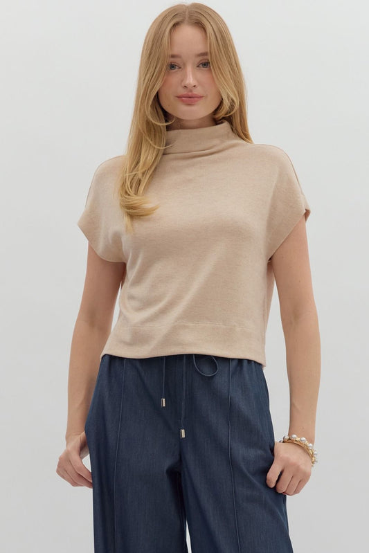 Woman wearing a beige turtleneck top and dark blue pants on a white background
