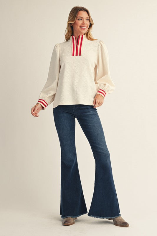 Woman wearing a cream blouse with red accents and blue jeans on a plain background
