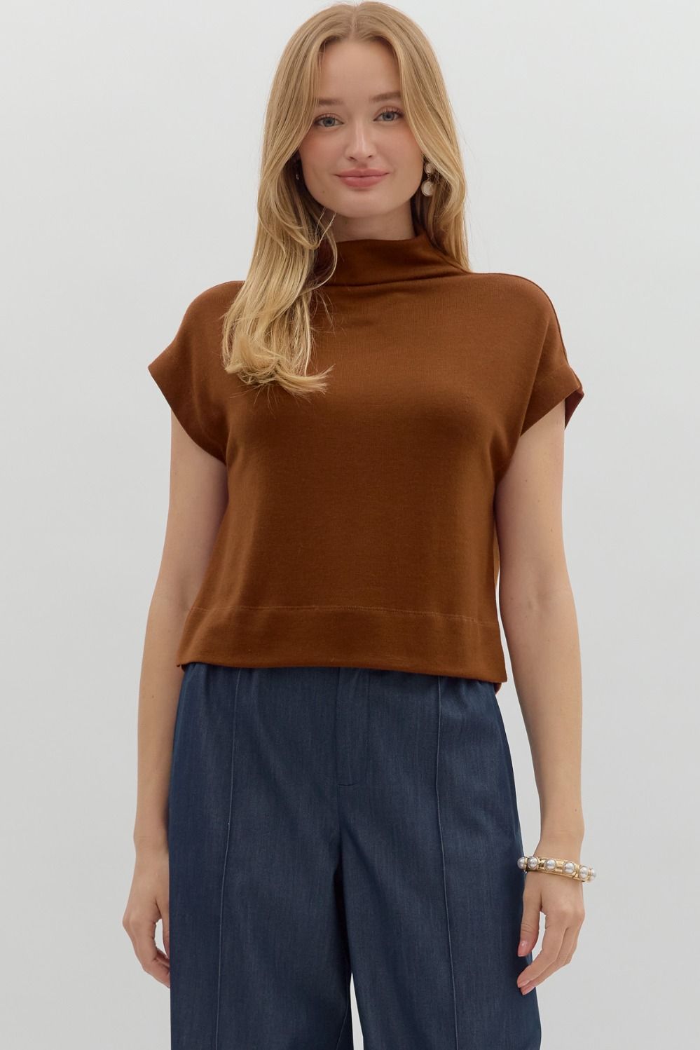 Woman wearing a brown sleeveless top and blue pants on a white background