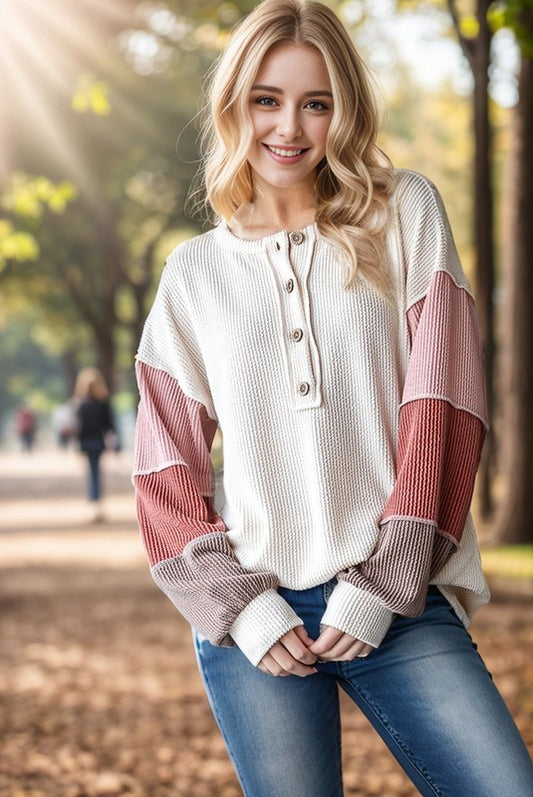 Woman wearing a white and pink long-sleeve shirt in an outdoor setting with trees and people in the background.