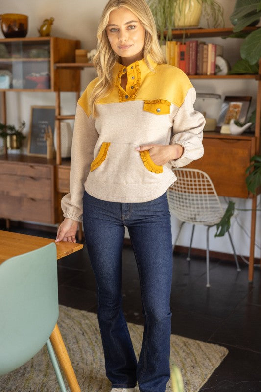 Woman wearing a yellow and beige shirt with blue jeans in a room with wooden furniture and plants.