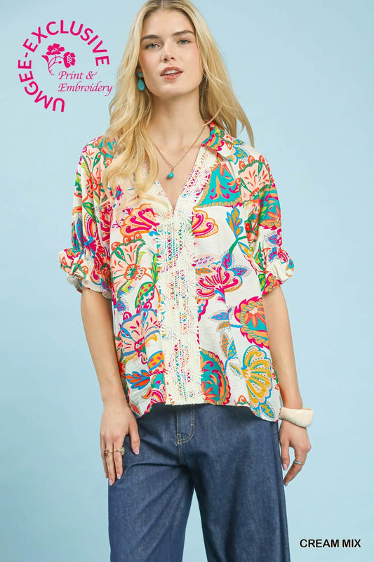woman wearing cream paisley boho top with colorful print, lace trim detail, split neckline, and short puff sleeves
