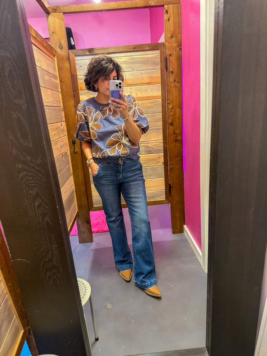 Person taking a mirror selfie wearing a floral top and blue jeans in a room with pink walls.