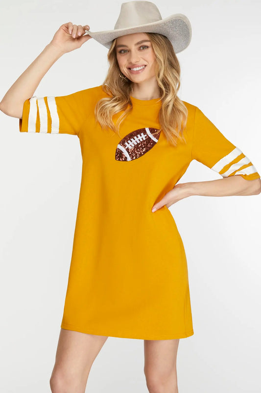 Woman wearing a mustard yellow dress with a football design and white sleeves on a white background