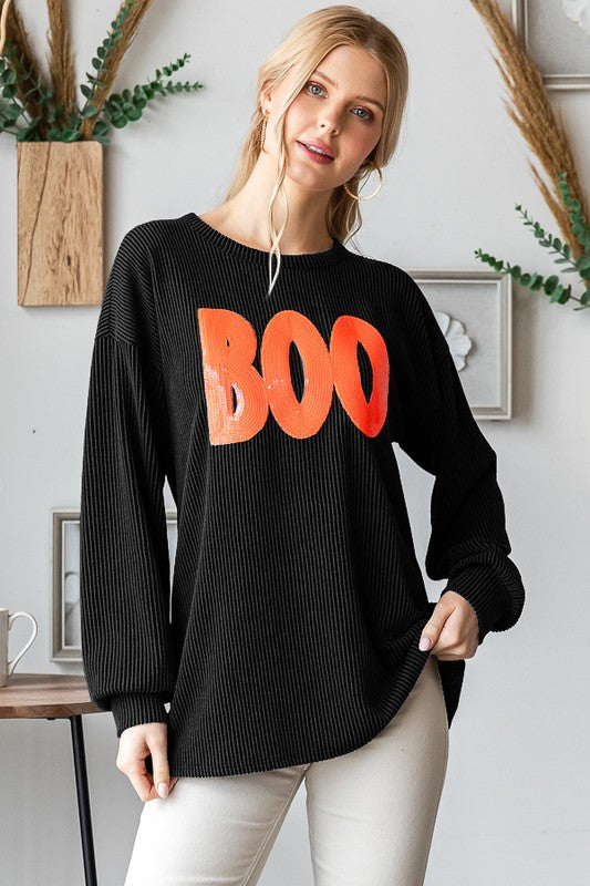 Woman wearing a black sweater with 'BOO' in orange text, standing in a room with decor elements.