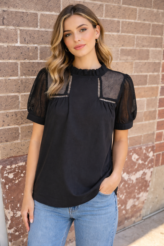 Black 100 percent cotton women’s top with sheer mesh neckline and puff sleeves styled with light wash denim
