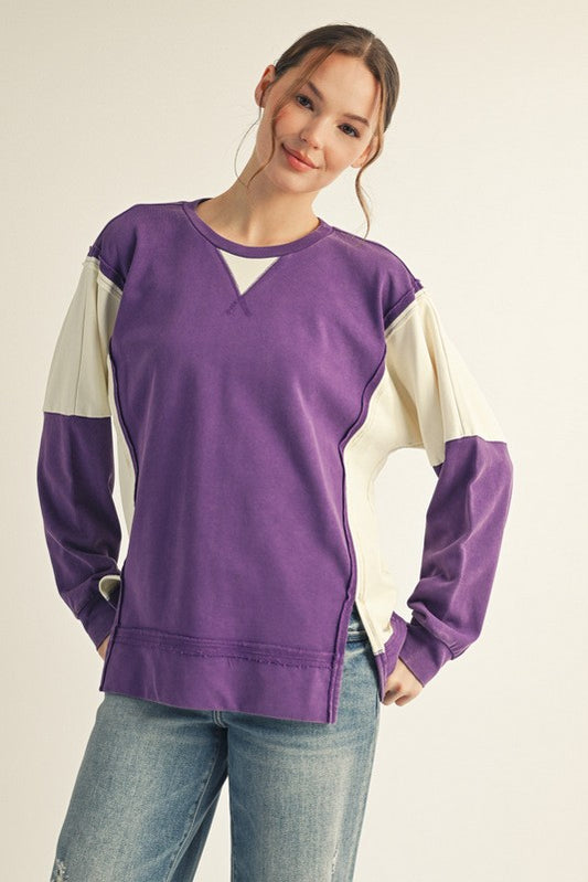 Woman wearing a purple and beige long-sleeve top with blue jeans on a plain background