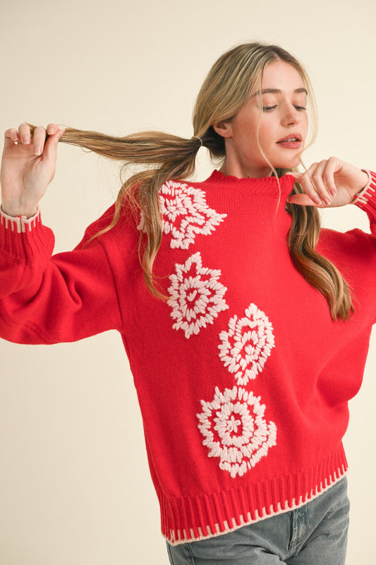 Woman wearing a red sweater with white floral patterns, holding her hair.