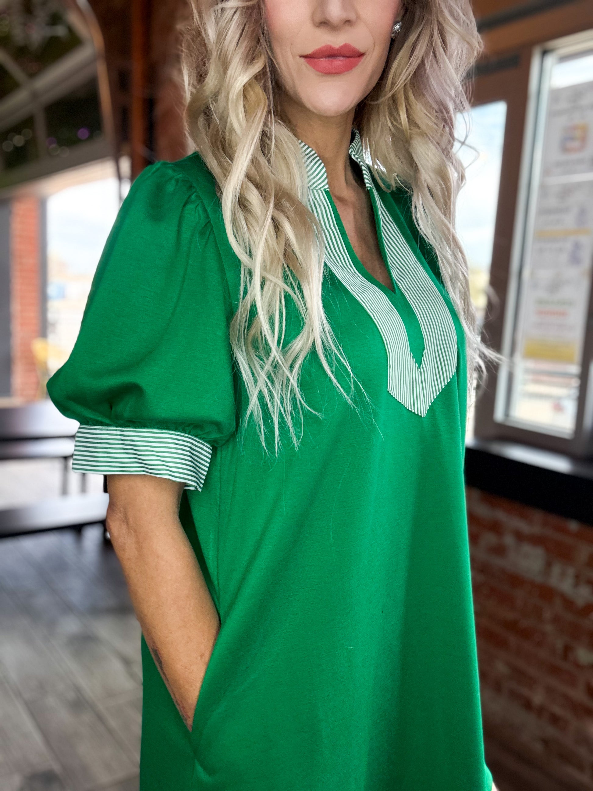 Woman wearing a green dress with a white collar in an indoor setting.